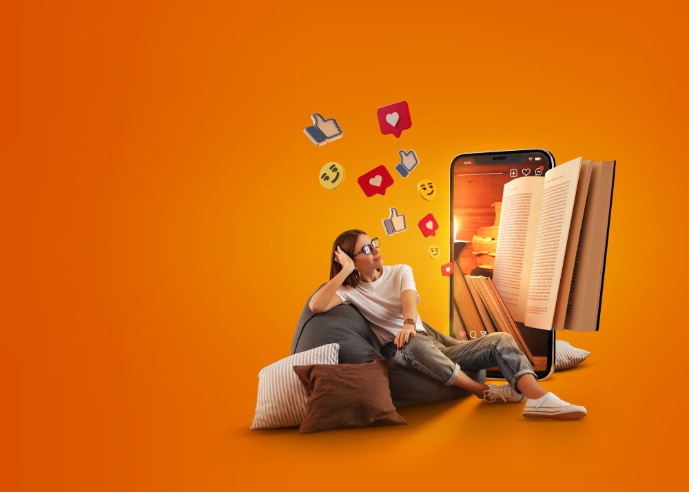 A woman sitting on a beanbag, with orange background wearing spectacles reading book and consuming Social media